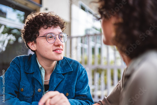 Young woman sitting at the table in an open-air restaurant, looking looking intensely at her girlfriend.