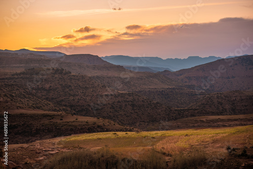 The sun setting over layers of mountains and a field of crops in rural Lesotho