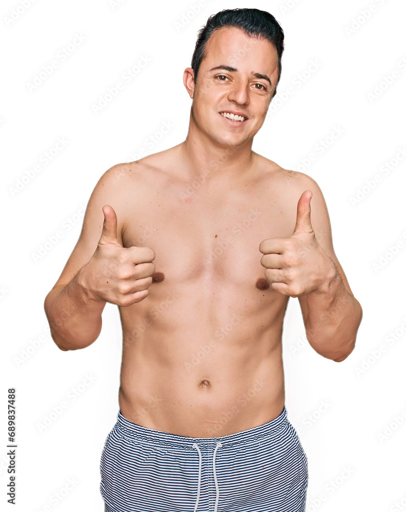 Handsome young man wearing swimwear shirtless success sign doing positive gesture with hand, thumbs up smiling and happy. cheerful expression and winner gesture.