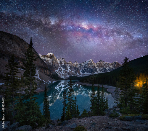View of Lake Moraine at night with the Milky Way galaxy visible in the sky, a beautiful lake with mountains and snow in Banff National Park, Alberta, Canada.