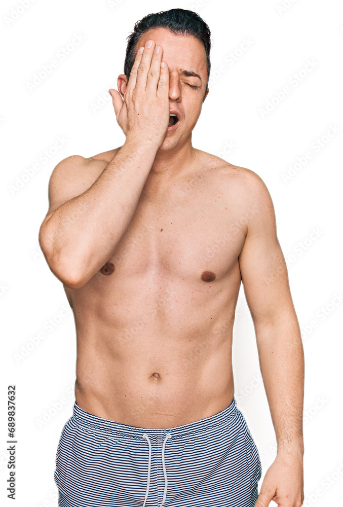 Fototapeta premium Handsome young man wearing swimwear shirtless yawning tired covering half face, eye and mouth with hand. face hurts in pain.