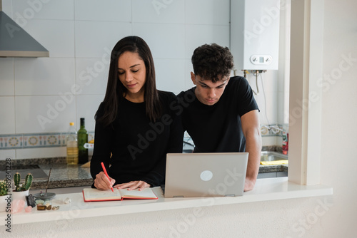 Positive young couple using laptop and writing notes