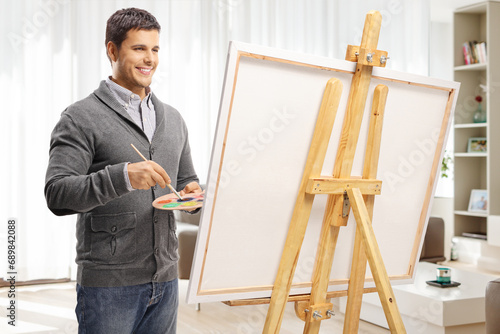 Handsome young man painting on a canvas at home