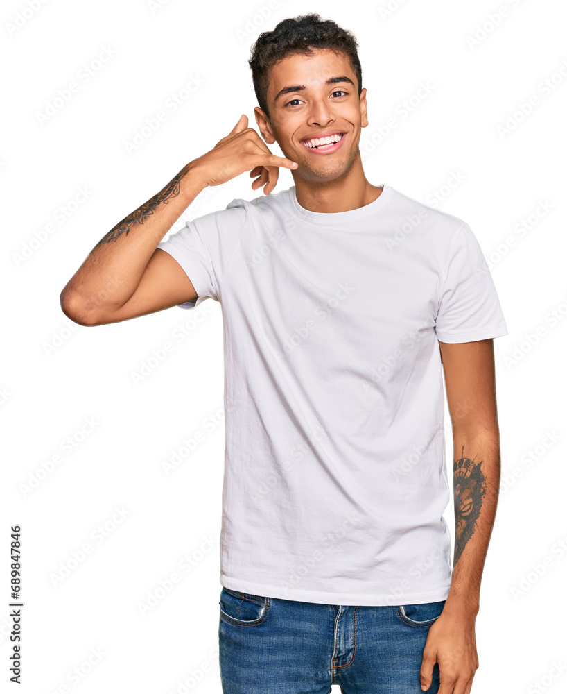Young handsome african american man wearing casual white tshirt smiling doing phone gesture with hand and fingers like talking on the telephone. communicating concepts. Young handsome african american man wearing casual white tshirt smiling doing phone gesture with hand and fingers like talking on the telephone. communicating concepts.