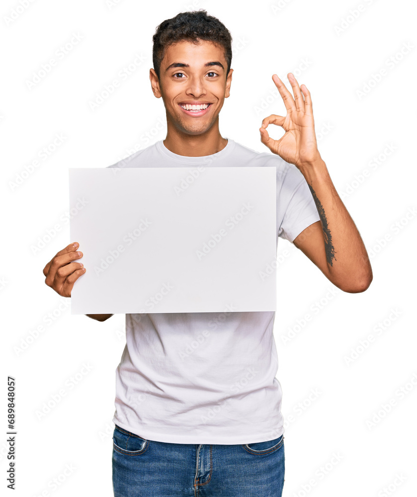 Young handsome african american man holding blank empty banner doing ok sign with fingers, smiling friendly gesturing excellent symbol