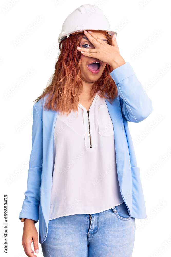 Young latin woman wearing architect hardhat peeking in shock covering face and eyes with hand, looking through fingers with embarrassed expression. Young latin woman wearing architect hardhat peeking in shock covering face and eyes with hand, looking through fingers with embarrassed expression.