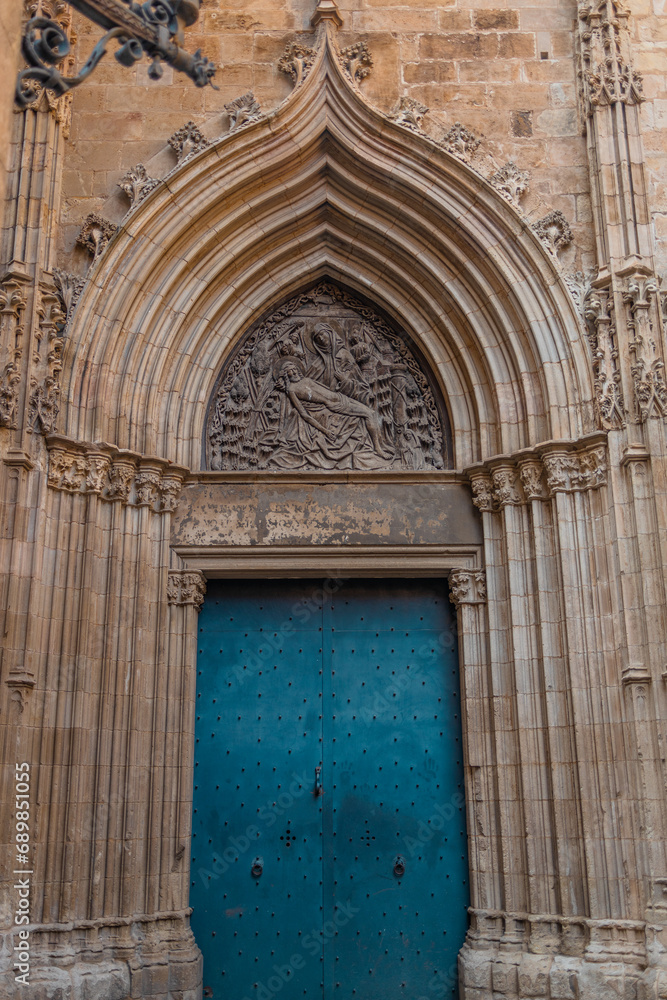 View of the old and beautiful art iron blue color door with doorknocker, classic architectural detail, stone semicircular arch with ornaments in the facade. Barcelona, Spain. 