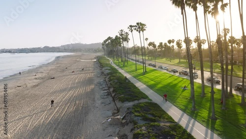 Aerial view of Santa Barbara coastline in sunset light, California, USA. Overhead shot of people enjoying vacation on the sandy beach. Sun rays breaking through the palm trees along road, 4k footage  photo