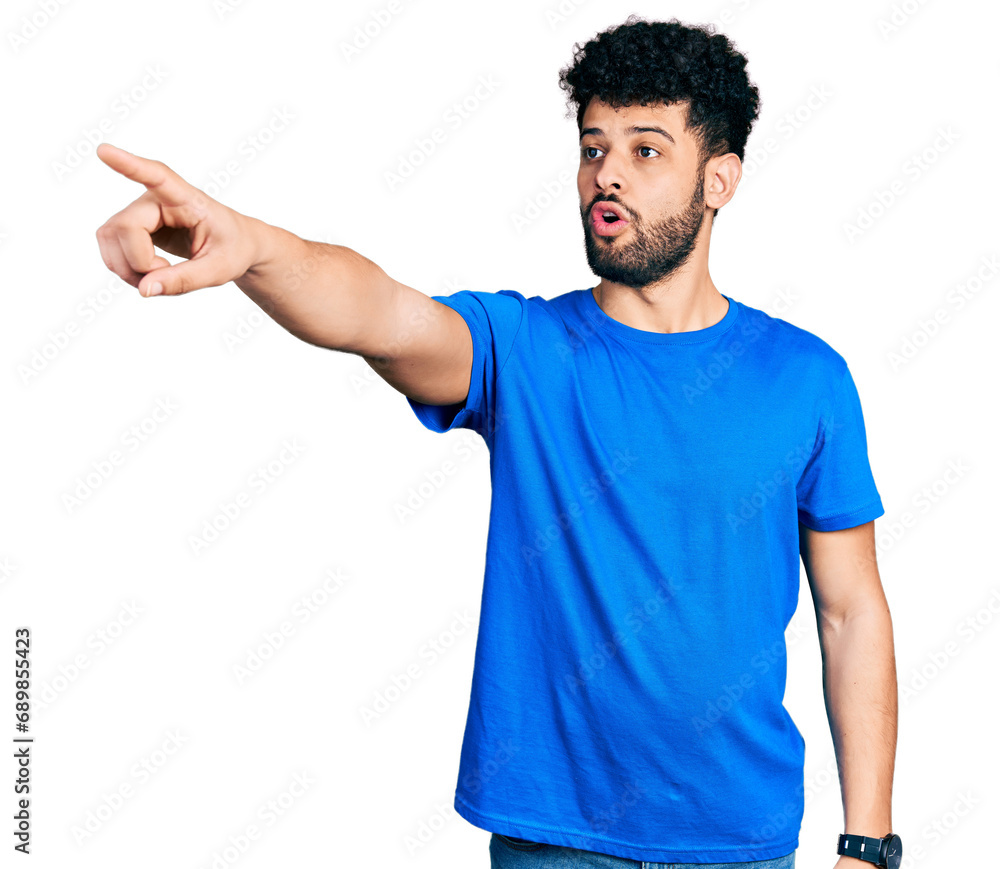 Young arab man with beard wearing casual blue t shirt pointing with finger surprised ahead, open mouth amazed expression, something on the front Young arab man with beard wearing casual blue t shirt pointing with finger surprised ahead, open mouth amazed expression, something on the front