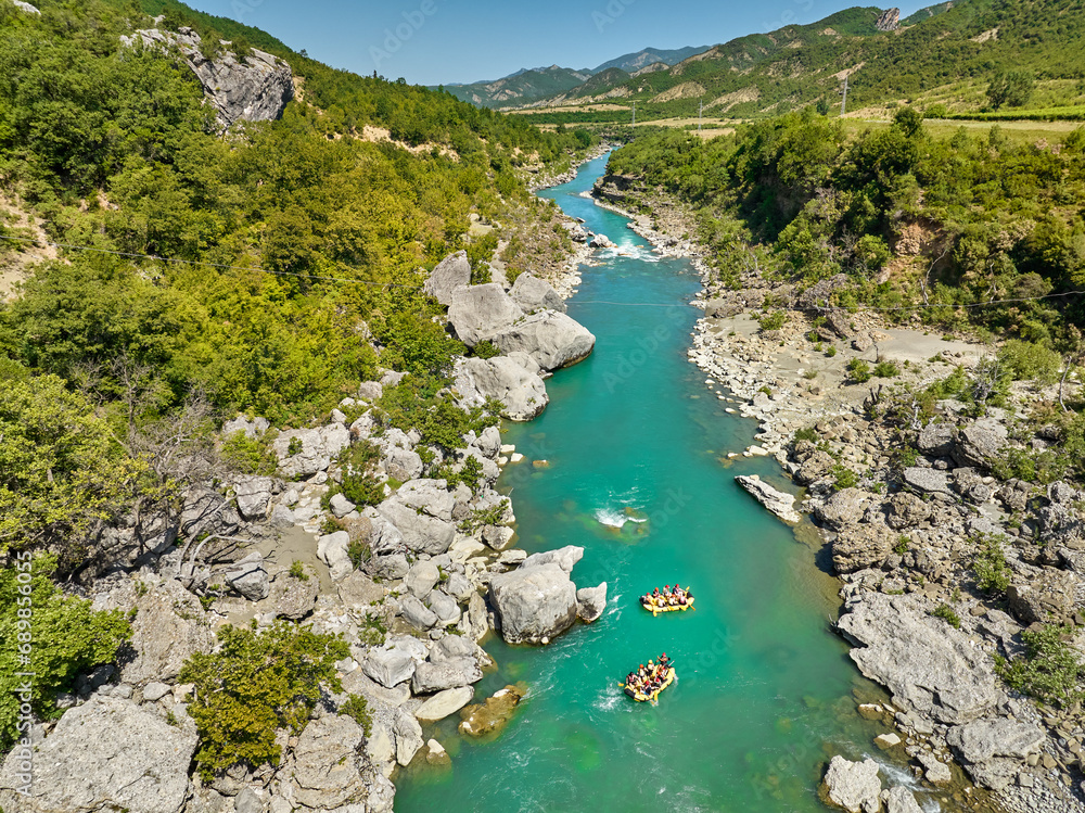 White water rafting. Adventure and sport. A yellow raft floating among the rocks on the crystal clear, blue-green water. Perpendicular drone view of the rafters floating on Vjose river, Albania. White water rafting. Adventure and sport. A yellow raft floating among the rocks on the crystal clear, blue-green water. Perpendicular drone view of the rafters floating on Vjose river, Albania.