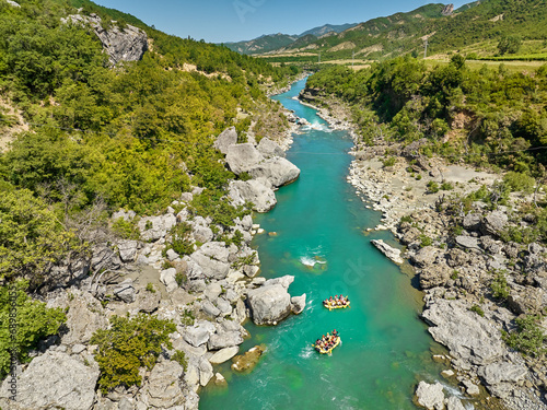 White water rafting. Adventure and sport. A yellow raft floating among the rocks on the crystal clear, blue-green water. Perpendicular drone view of the rafters floating on Vjose river, Albania.