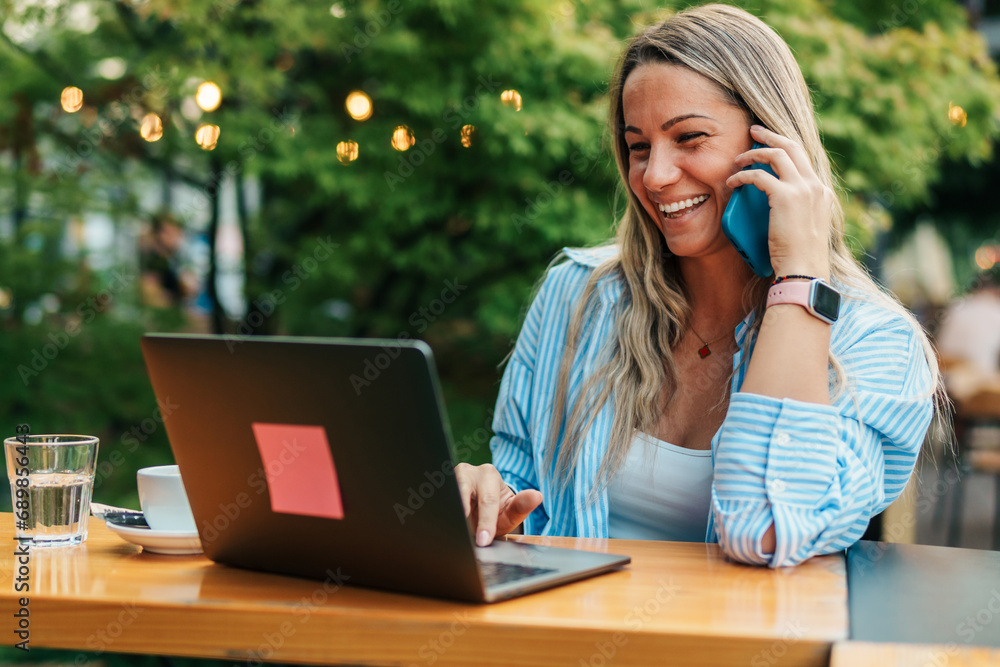 Seated in the café's garden, a businesswoman efficiently coordinates her call and online work, ensuring the seamless exchange of information with her business counterpart. Seated in the café's garden, a businesswoman efficiently coordinates her call and online work, ensuring the seamless exchange of information with her business counterpart.