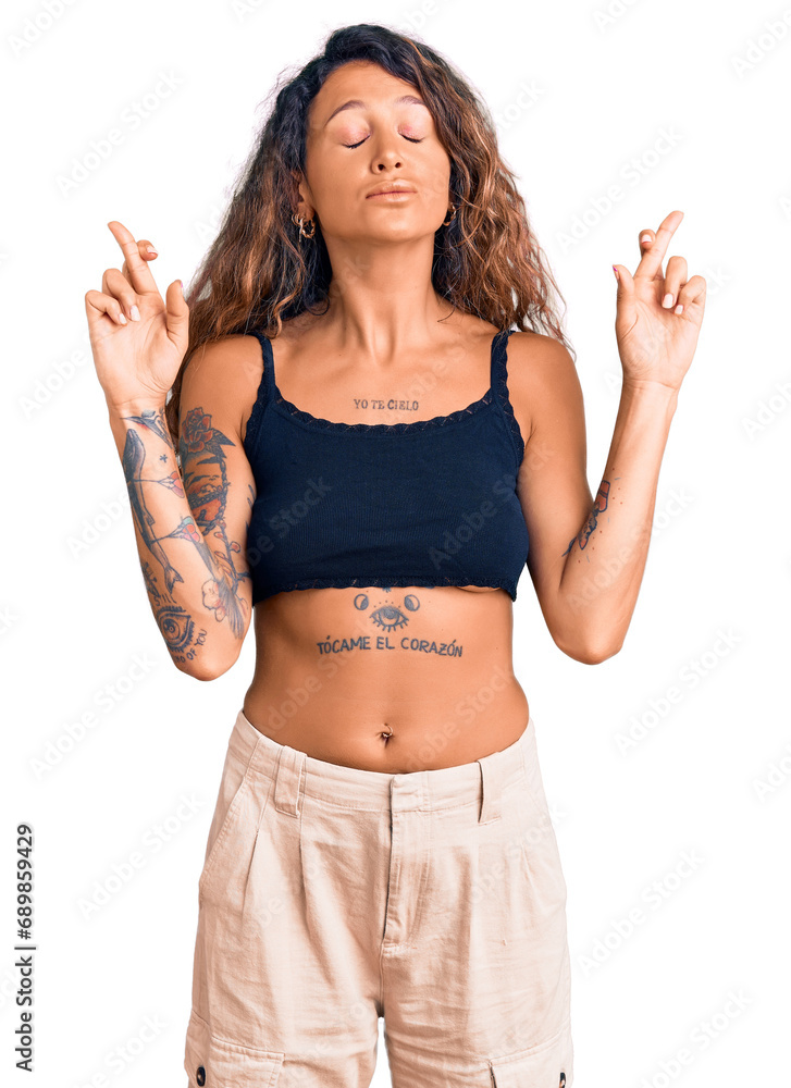 Young hispanic woman with tattoo wearing casual clothes gesturing finger crossed smiling with hope and eyes closed. luck and superstitious concept. Young hispanic woman with tattoo wearing casual clothes gesturing finger crossed smiling with hope and eyes closed. luck and superstitious concept.