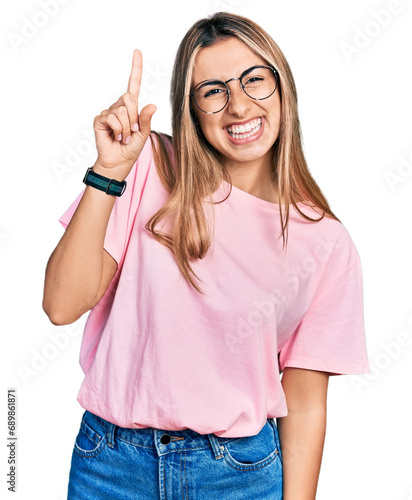 Hispanic young woman wearing casual t shirt and glasses pointing finger up with successful idea. exited and happy. number one.