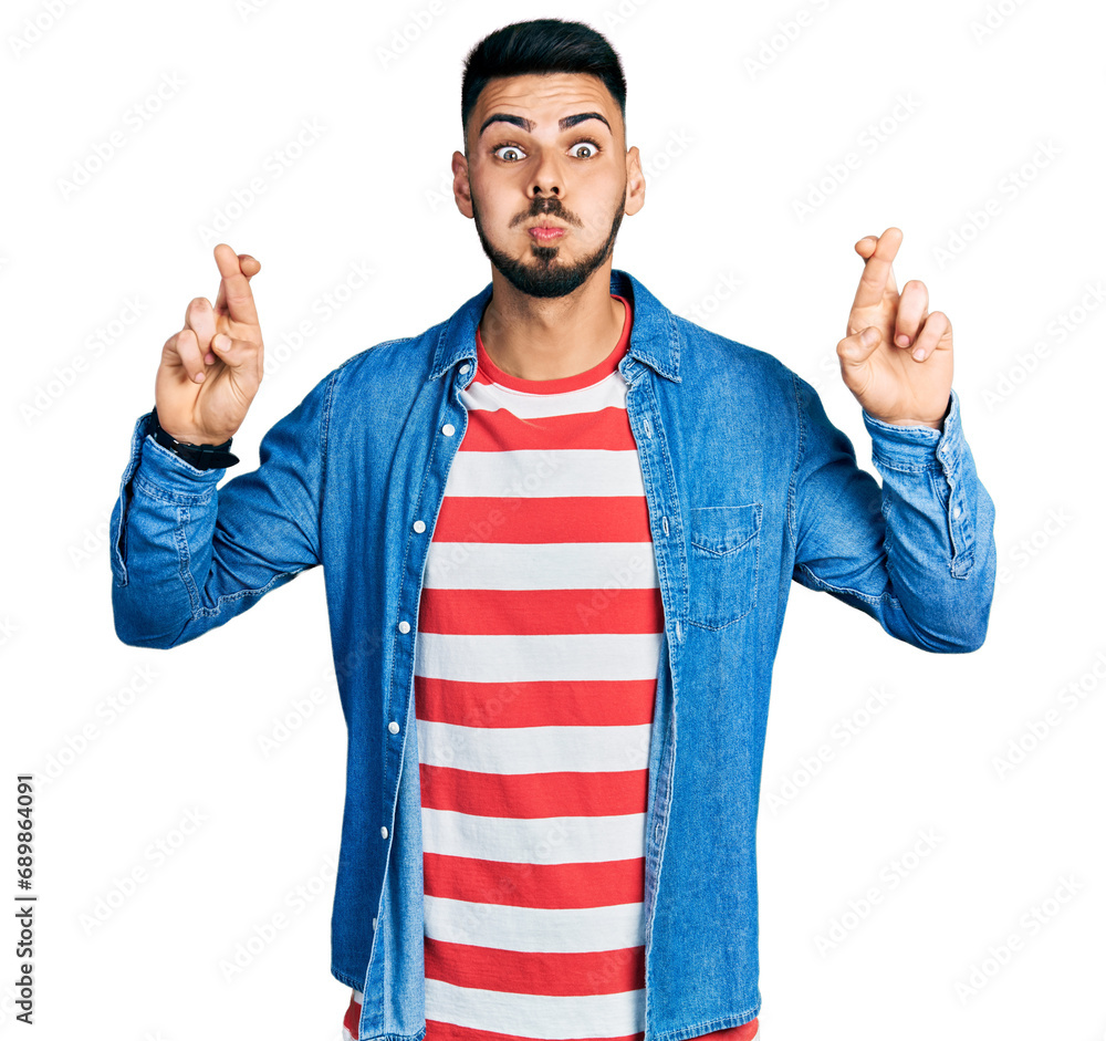 Young hispanic man with beard doing fingers crossed luck gesture puffing cheeks with funny face. mouth inflated with air, catching air. Young hispanic man with beard doing fingers crossed luck gesture puffing cheeks with funny face. mouth inflated with air, catching air.