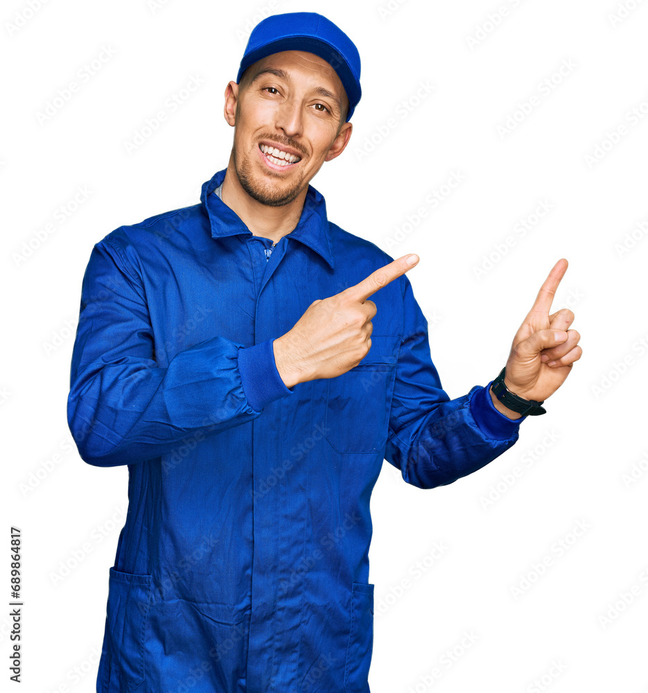 Bald man with beard wearing builder jumpsuit uniform smiling and looking at the camera pointing with two hands and fingers to the side. Bald man with beard wearing builder jumpsuit uniform smiling and looking at the camera pointing with two hands and fingers to the side.
