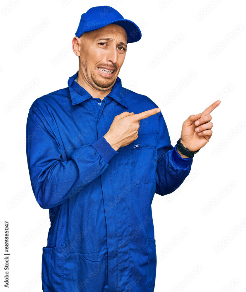 Bald man with beard wearing builder jumpsuit uniform pointing aside worried and nervous with both hands, concerned and surprised expression Bald man with beard wearing builder jumpsuit uniform pointing aside worried and nervous with both hands, concerned and surprised expression