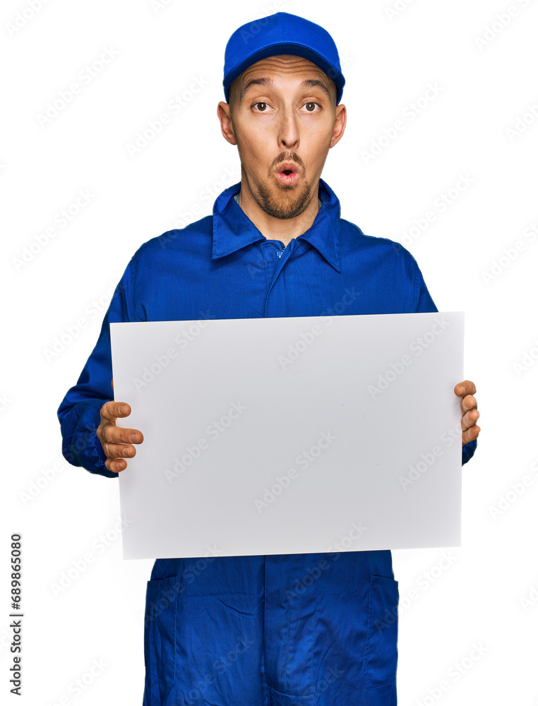 Bald man with beard wearing builder jumpsuit uniform holding empty banner scared and amazed with open mouth for surprise, disbelief face Bald man with beard wearing builder jumpsuit uniform holding empty banner scared and amazed with open mouth for surprise, disbelief face