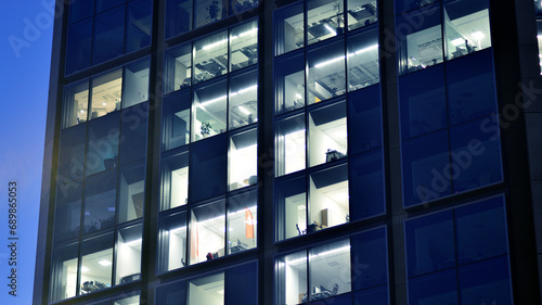 Fragment of the glass facade of a modern corporate building at night. Modern glass office in city. Big glowing windows in modern office buildings at night, in rows of windows light shines. 