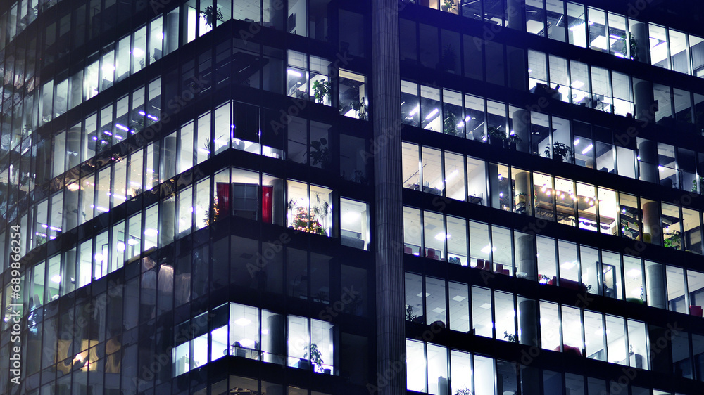 Fragment of the glass facade of a modern corporate building at night. Modern glass office in city. Big glowing windows in modern office buildings at night, in rows of windows light shines. Fragment of the glass facade of a modern corporate building at night. Modern glass office in city. Big glowing windows in modern office buildings at night, in rows of windows light shines.