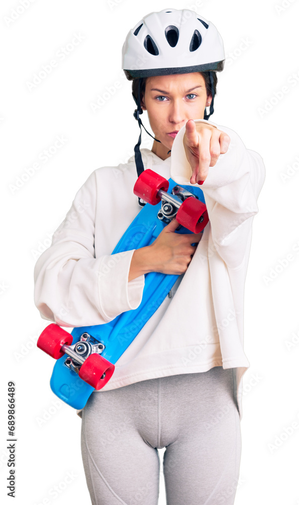 Beautiful brunette young woman wearing safety helmet and skate pointing with finger to the camera and to you, confident gesture looking serious Beautiful brunette young woman wearing safety helmet and skate pointing with finger to the camera and to you, confident gesture looking serious