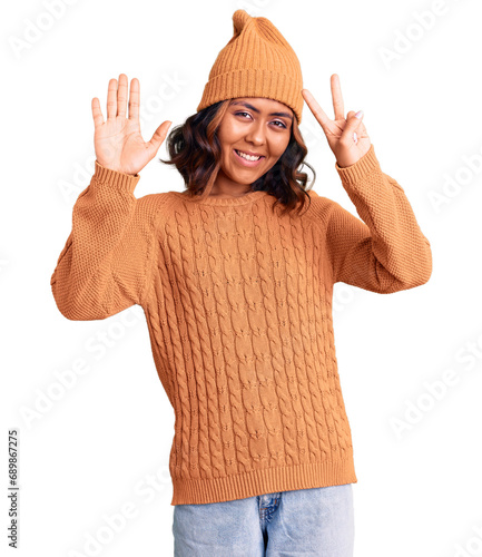 Young beautiful mixed race woman wearing wool sweater and winter hat showing and pointing up with fingers number seven while smiling confident and happy. photo