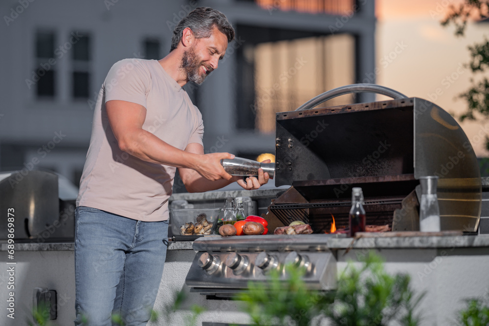 Man at a barbecue grill. Male cook preparing barbecue outdoors. Bbq meat, grill for picnic. Roasted beef. Cook preparing barbeque in the house yard. Barbecue and grill. Cook using barbecue tongs. Man at a barbecue grill. Male cook preparing barbecue outdoors. Bbq meat, grill for picnic. Roasted beef. Cook preparing barbeque in the house yard. Barbecue and grill. Cook using barbecue tongs.