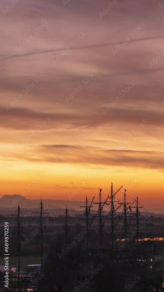 Vertical video. Sunrise At A Seaside Dock With Sailboats Moored Along The Shore. The Sun Rises Behind The Hills, Painting The Sky In Fiery Shades Of Red. Vertical video. Sunrise At A Seaside Dock With Sailboats Moored Along The Shore. The Sun Rises Behind The Hills, Painting The Sky In Fiery Shades Of Red.