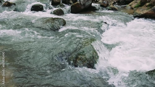 Mountain creek swiftly flowing over stones, natural rapid stream. Creek rushing over stones in clear mountain setting. Stone-lined creek in mountains, clear water flowing rapidly photo