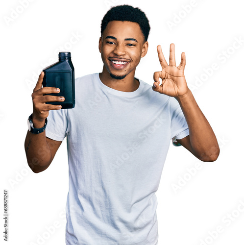 Young african american man holding motor oil bottle doing ok sign with fingers, smiling friendly gesturing excellent symbol