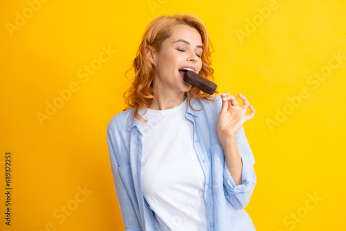 Portrait of cheerful funny teenage girl enjoys eating cold frozen dessert, eats delicious chocolate ice cream, yellow background. Female model enjoy ice-cream.