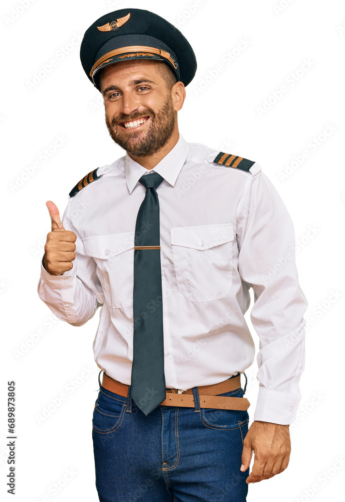 Handsome man with beard wearing airplane pilot uniform doing happy thumbs up gesture with hand. approving expression looking at the camera showing success. Handsome man with beard wearing airplane pilot uniform doing happy thumbs up gesture with hand. approving expression looking at the camera showing success.
