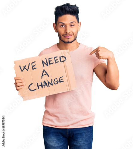 Handsome latin american young man holding we need a change banner pointing finger to one self smiling happy and proud