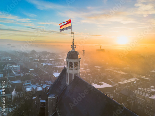 Drone view across town of Sneek with Dutch flag on top of a church at sunrise photo