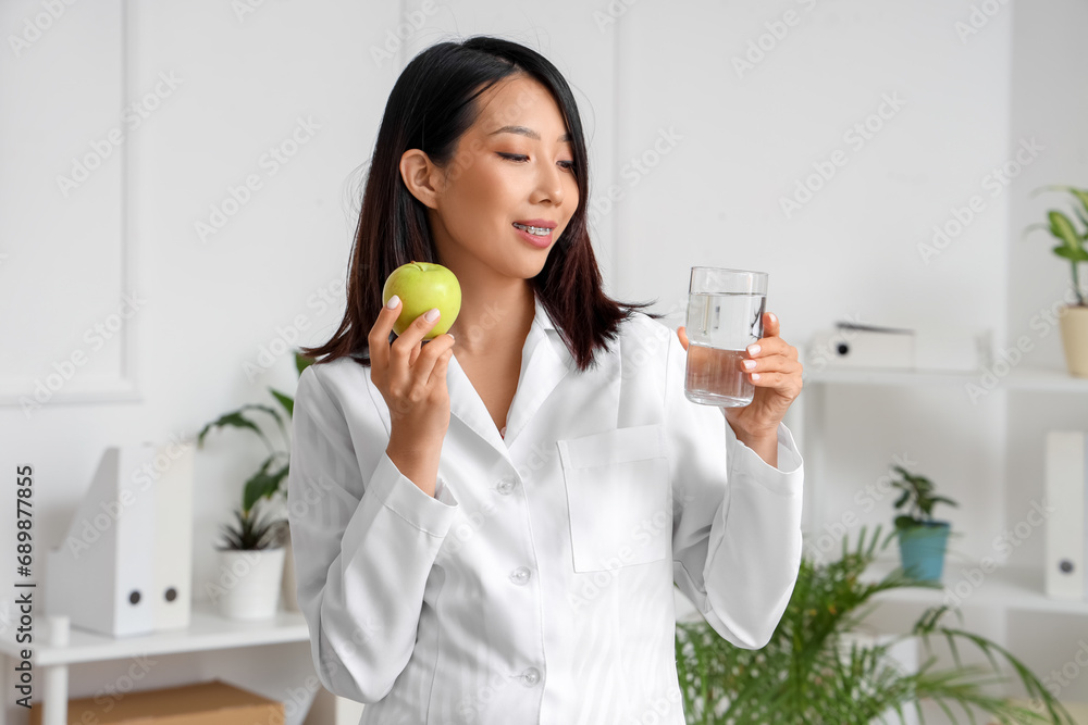 Female Asian nutritionist with apple and glass of water in office Female Asian nutritionist with apple and glass of water in office