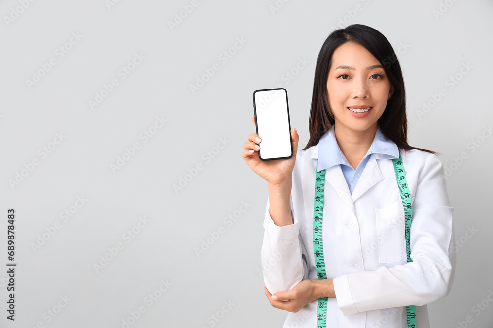 Female Asian nutritionist with mobile phone on light background Female Asian nutritionist with mobile phone on light background