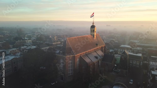 Drone view across town of Sneek with Dutch flag on top of a church at sunrise photo