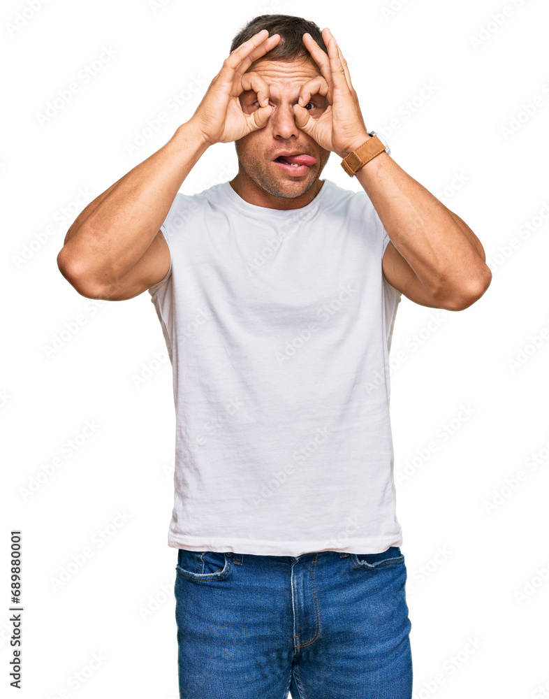Handsome muscle man wearing casual white tshirt doing ok gesture like binoculars sticking tongue out, eyes looking through fingers. crazy expression. Handsome muscle man wearing casual white tshirt doing ok gesture like binoculars sticking tongue out, eyes looking through fingers. crazy expression.