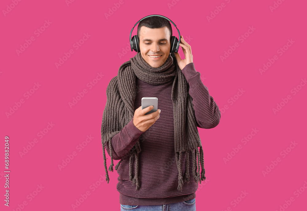 Young man in winter clothes with headphones using mobile phone on purple background Young man in winter clothes with headphones using mobile phone on purple background
