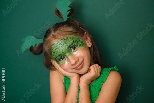 A cute beautiful girl with makeup with a painted dragon and gold sequins on her cheeks. A headdress in the shape of green dragon wings. New Year 2024