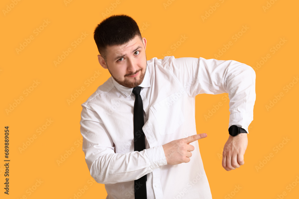 Young businessman pointing at wrist watch on yellow background. Time management concept Young businessman pointing at wrist watch on yellow background. Time management concept