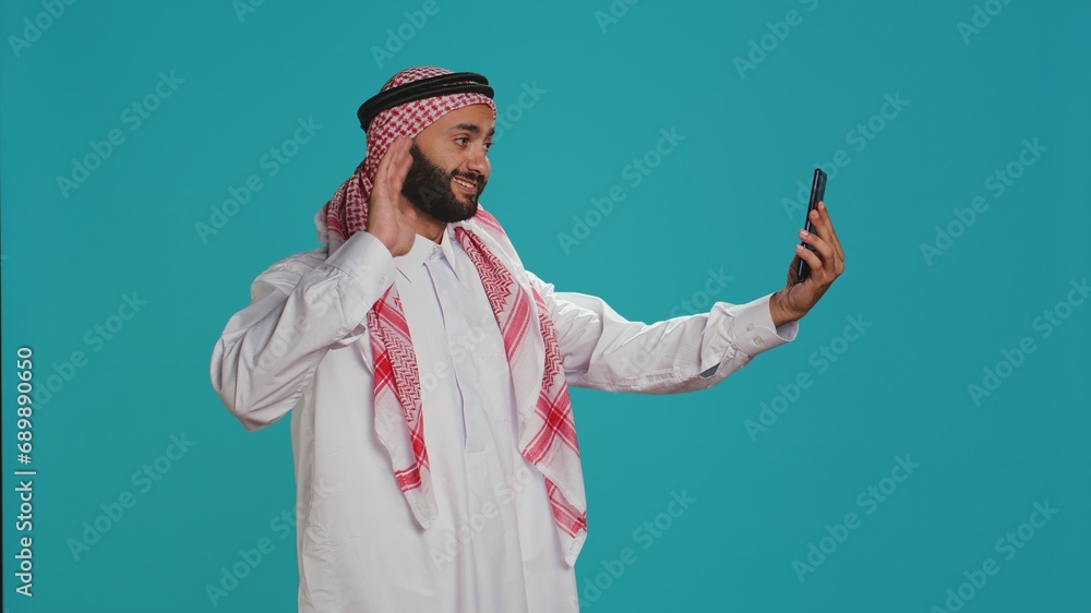 Arab person greeting people on call, waving and catching up with friends on remote network connection. Middle eastern adult in traditional islamic clothing discussing on teleconference. Arab person greeting people on call, waving and catching up with friends on remote network connection. Middle eastern adult in traditional islamic clothing discussing on teleconference.