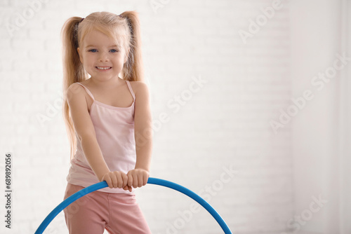 Cute little girl with hula hoop doing gymnastics in gym