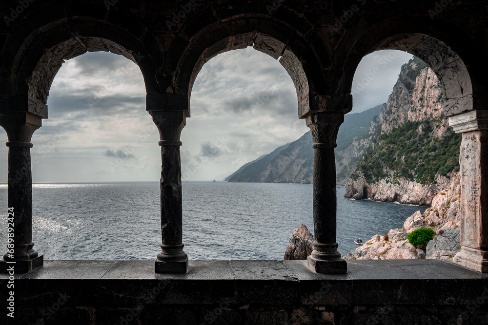 Arched stone window or opening in a stone wall overlooking scenic landscape of ligurian sea and mountains in Portovenere, Italy.