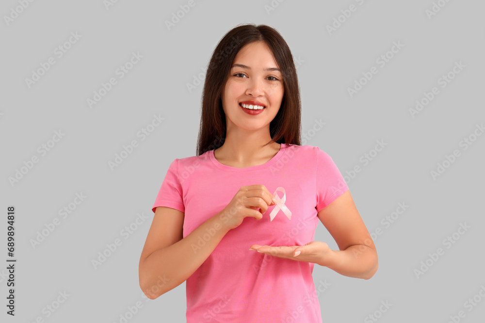 Young Asian woman with pink ribbon on light background. Breast cancer awareness concept Young Asian woman with pink ribbon on light background. Breast cancer awareness concept