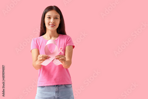 Young Asian woman with pink ribbons on color background. Breast cancer awareness concept