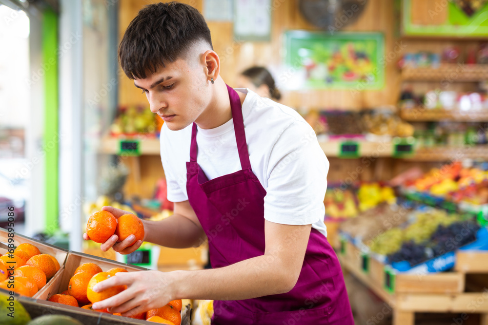 Hardworking young salesman working in a vegetable store puts fresh oranges on the counter for sale