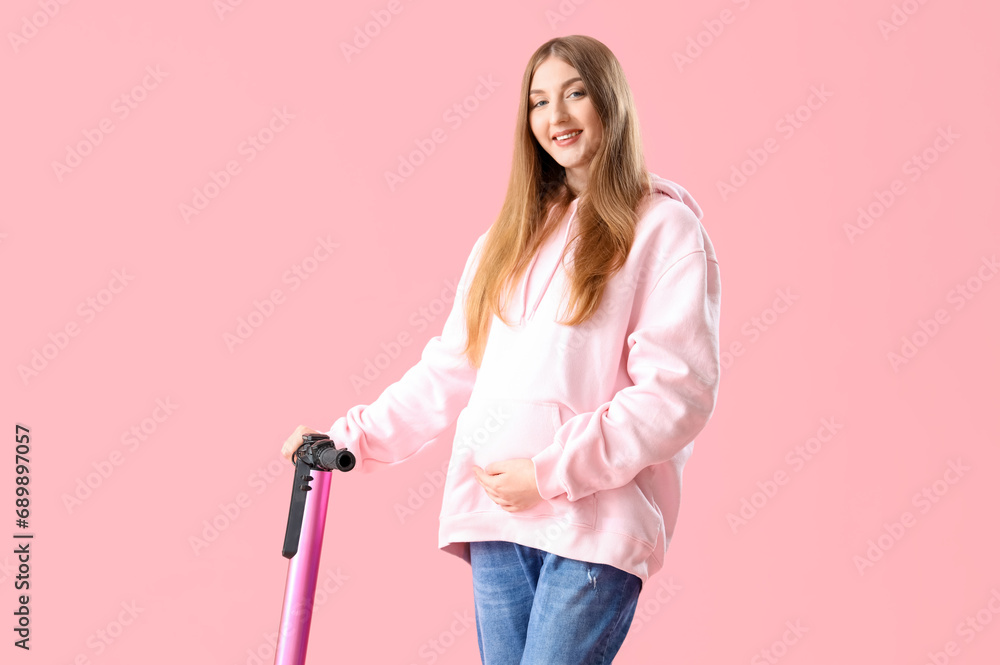 Beautiful young pregnant woman with electric kick scooter on pink background