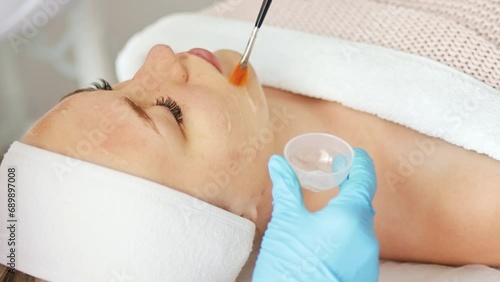 Beautician cosmetologist applies cosmetic product gel peeling mask, professional procedure in a beauty clinic salon for client. Skincare and cosmetology spa concept.	 photo