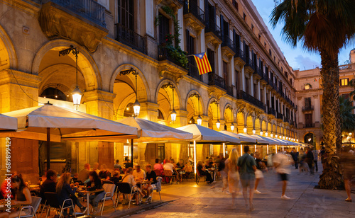 Nightlife at Placa Reial in Barcelona. Illuminated central city square crowded with people enjoying walks and relaxing in sidewalk cafes. Popular meeting point for locals and tourists